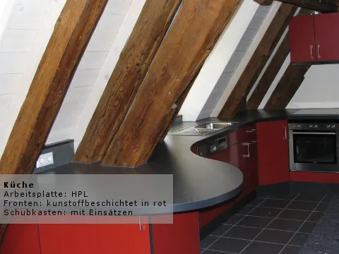 Küche mit roter Front unter einer Dachschräge mit sichtbaren Holzbalken