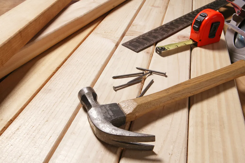 Hammer, Zollstock und Nägel auf hellen Holzlatten